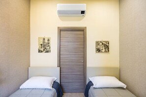 Une chambre d’hôtel avec deux lits, une porte, un appareil de climatisation et deux tableaux encadrés accrochés aux murs.