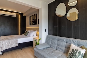 Una camera da letto moderna con un letto, un divano grigio e tre specchi fissati alla parete.
