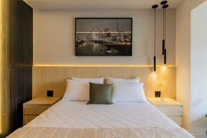Ein modernes Hotelzimmer mit einem großen Bett, einem Stadtbild über dem Kopfteil und einem Nachttisch mit einer Lampe.