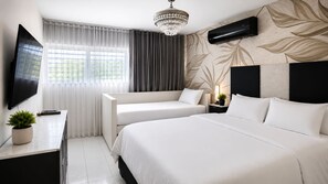 A hotel room with a bed, a sofa, a TV, a chandelier, and a wall-mounted air conditioner. - Exclusive Beachfront Retreat With Private Pool in Loíza, Puerto Rico (Loiza)