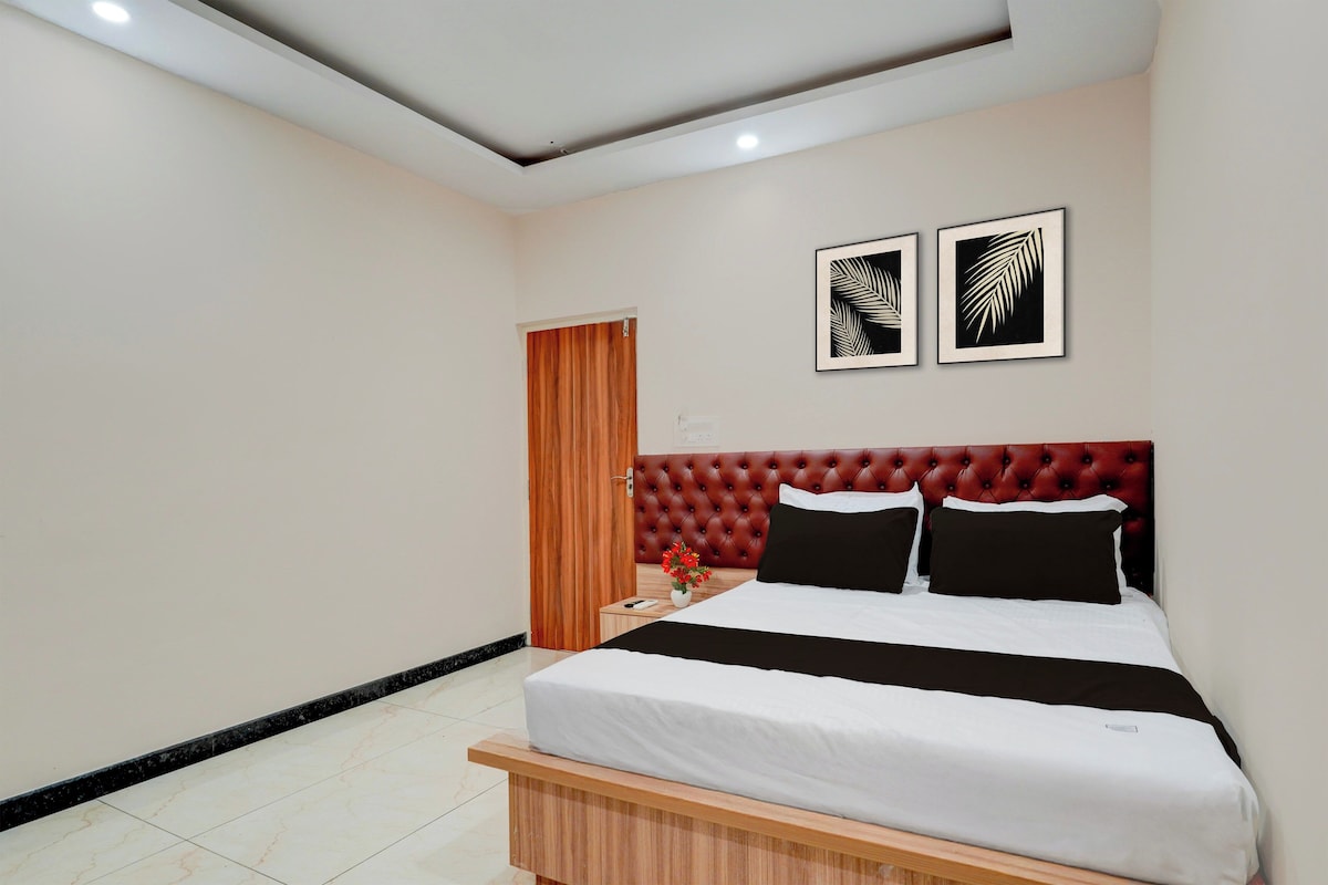 Habitació d'hotel amb un llit, una taula de nit, un panell de capçal tapissat de vermell i dues làmines penjades a la paret.