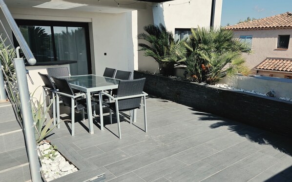 An outdoor patio with a glass-top table and chairs, surrounded by a low stone wall and potted plants.