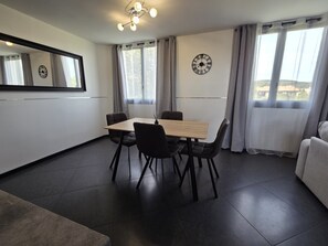 A modern dining area with a wooden table and black chairs, a wall clock, and a large window with curtains.