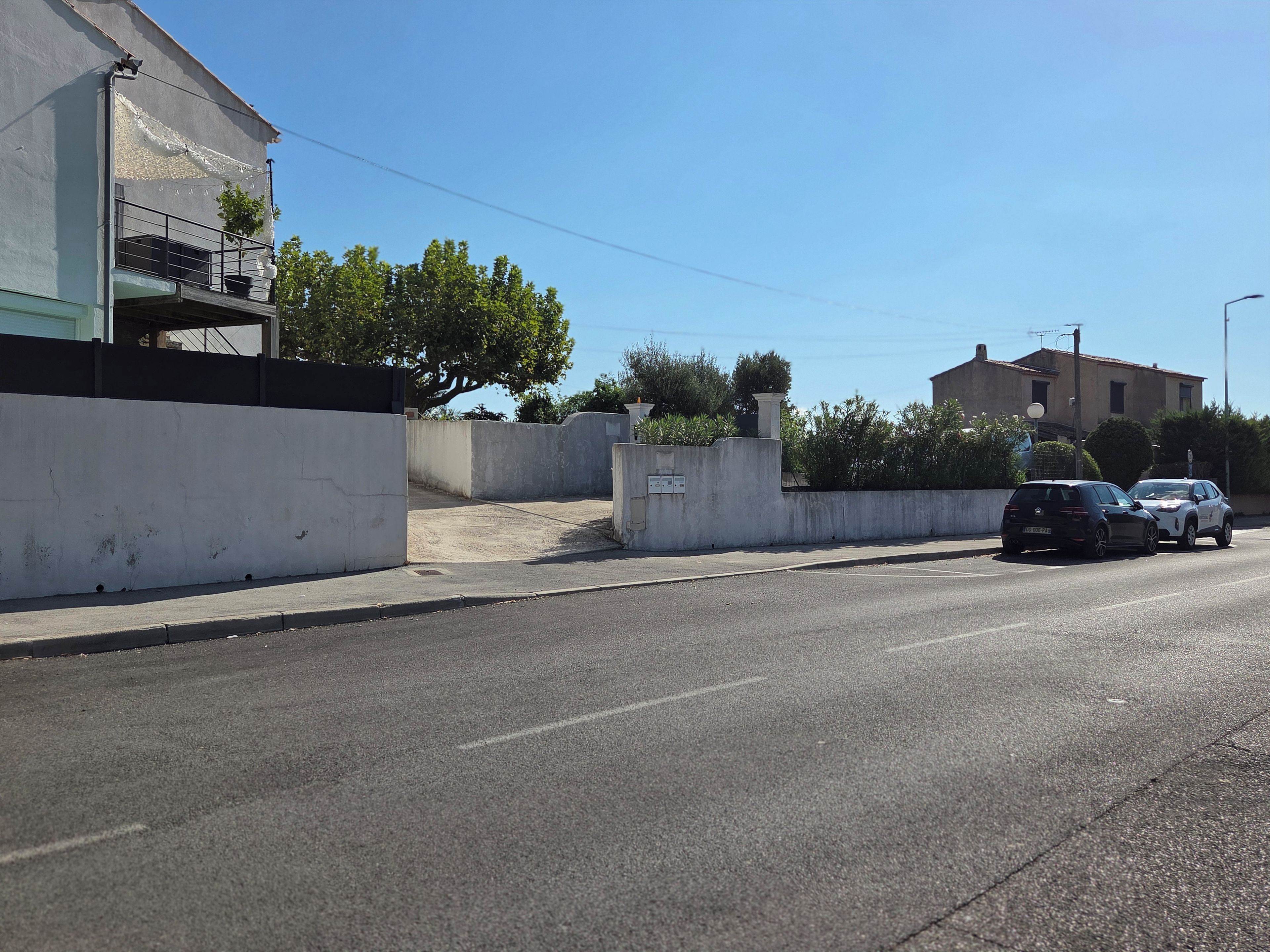 Une rue avec un immeuble blanc, une voiture noire et une voiture blanche garées sur le bord.
