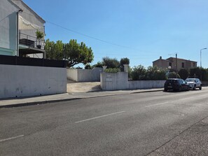 A street with a white building, a black car, and a white car parked on the side.