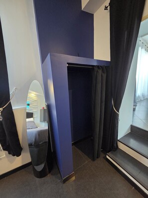 A room with a bed, a mirror, a dark-colored partition, and a staircase leading to an upper level.