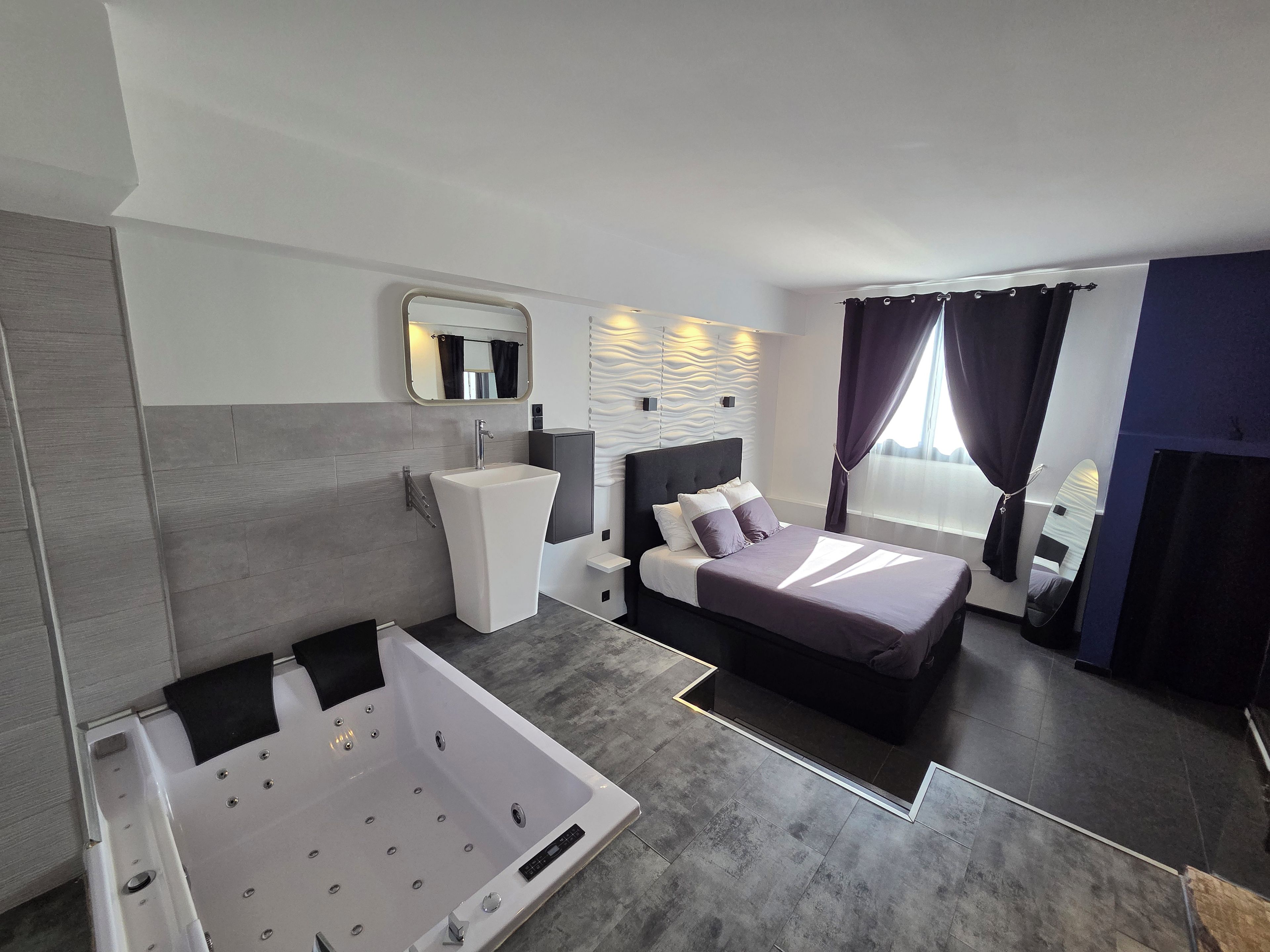 Una habitación de hotel moderna con una cama grande, un baño independiente con bañera y un ventanal con cortinas.