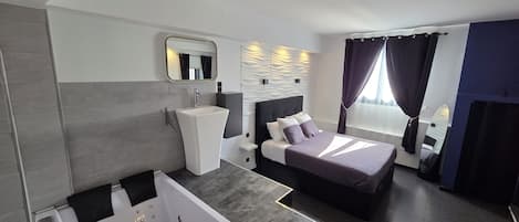 Une chambre d’hôtel moderne avec un grand lit, une salle de bain séparée avec une baignoire et une grande fenêtre avec des rideaux.
