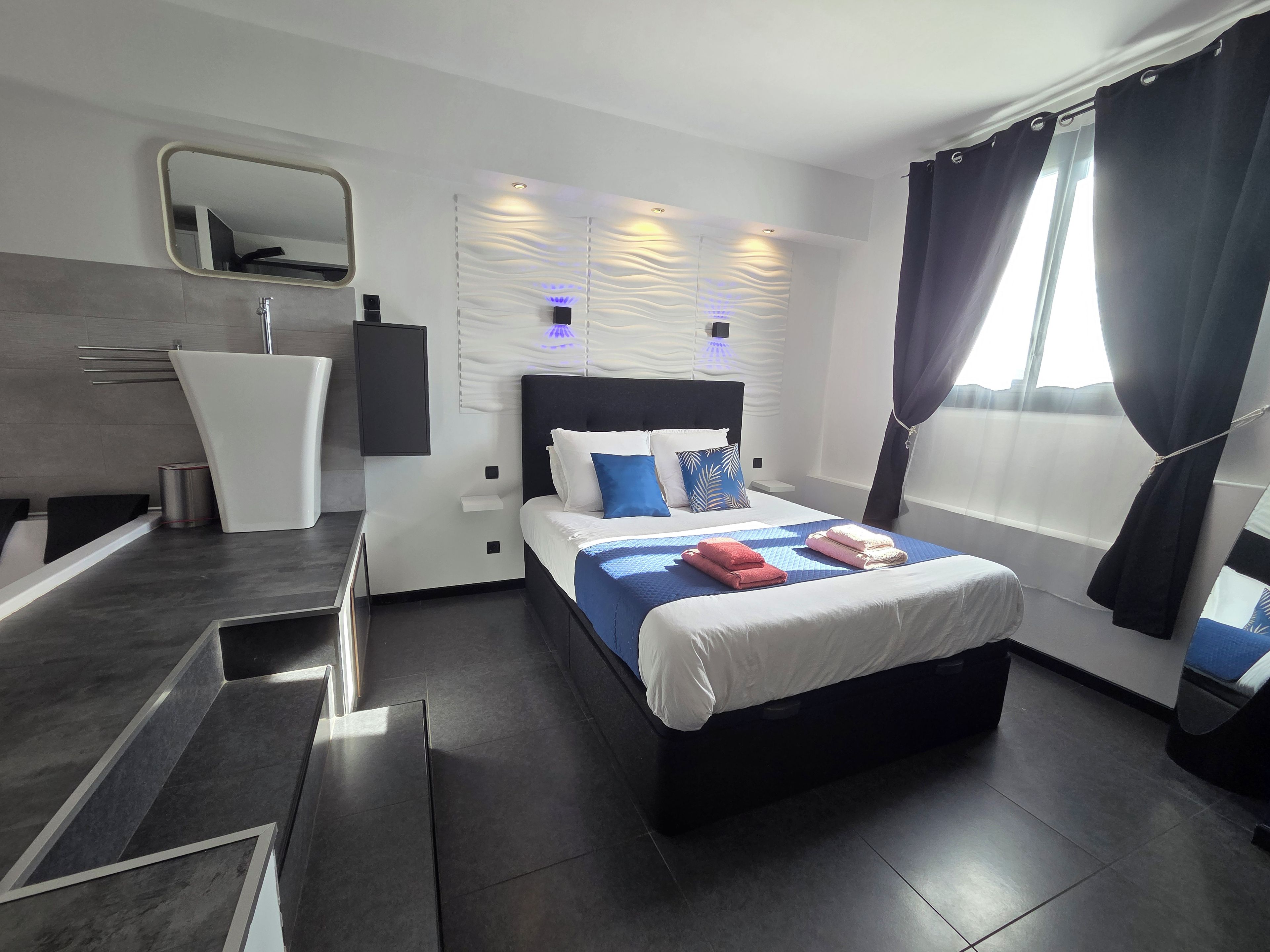 Une chambre d’hôtel moderne avec un grand lit, une table de chevet, un miroir et un luminaire fixé au mur.