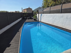 Een rechthoekig zwembad met helderblauw water, omgeven door een houten terras en een lage muur.