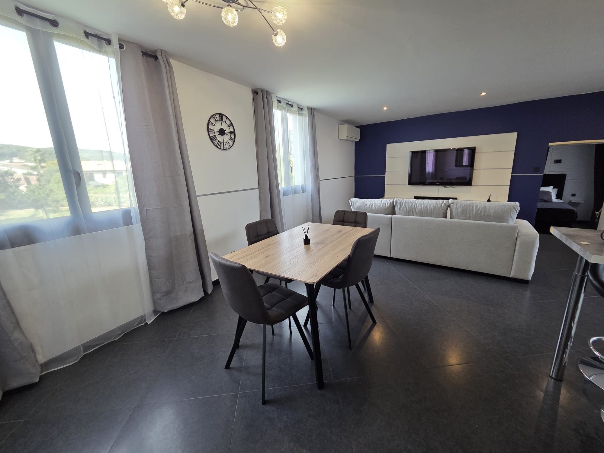 Un salon moderne comprenant un coin repas, un canapé, un téléviseur et une vue dégagée grâce à de grandes fenêtres.