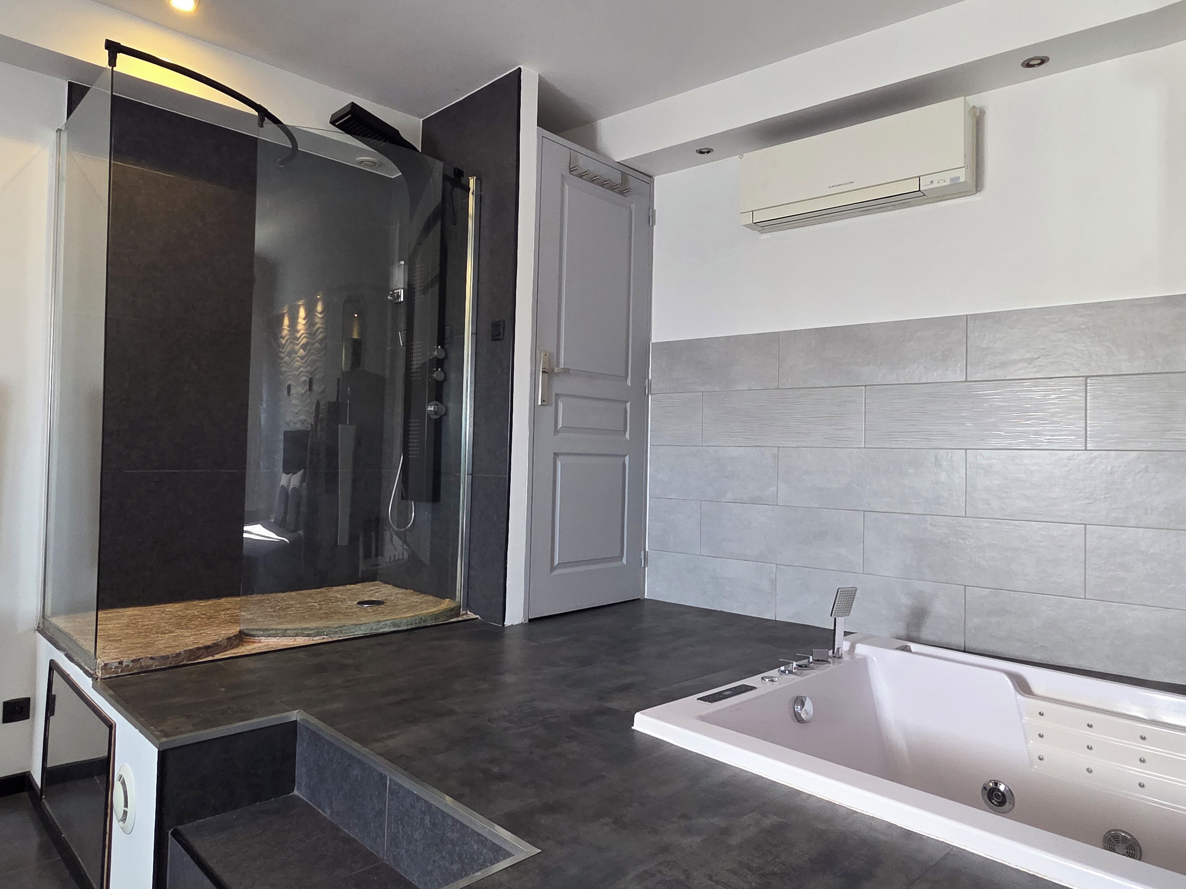 Ein modernes Badezimmer mit einer begehbaren Glasdusche, einer Badewanne und einer Fliesenwand.
