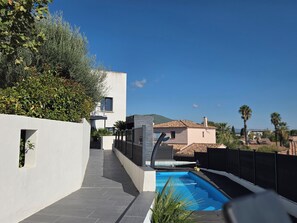 A modern outdoor pool area with a clear sky, a pathway leading to a building, and a view of a distant house.