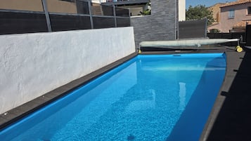 En swimmingpool med kristallklart blått vatten, omgiven av en vit vägg och en stenmur.