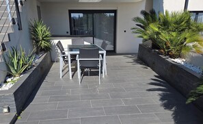 An outdoor patio with a table and chairs, surrounded by plants and a stone floor.