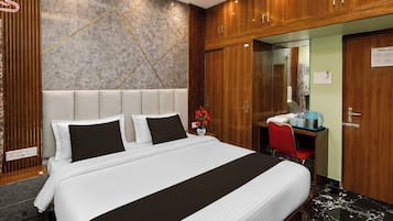Quarto de hotel com cama grande, escrivaninha, cadeira, espelho e guarda-roupa de madeira.