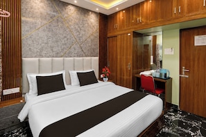 Ein Hotelzimmer mit einem großen Bett, einem Schreibtisch mit Stuhl, einem Spiegel und einem Holzschrank.