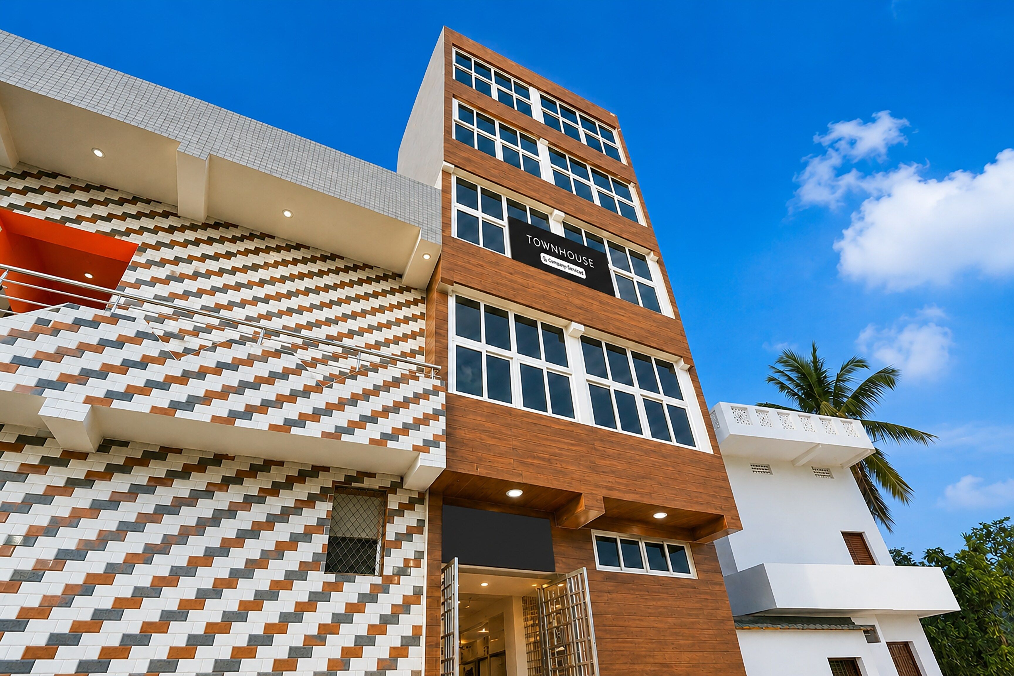 Un edificio de varios pisos con una fachada mixta de diseños y superficies lisas, un cartel llamativo que dice 'TOWNHOUSE' y un cielo azul despejado al fondo.
