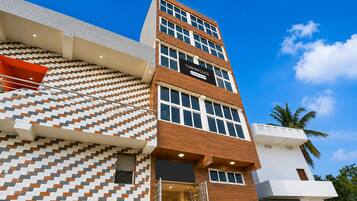 Un edificio de varios pisos con una fachada mixta de diseños y superficies lisas, un cartel llamativo que dice 'TOWNHOUSE' y un cielo azul despejado al fondo.