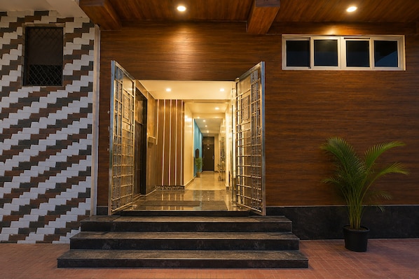 A modern hotel entrance with a wooden ceiling, a patterned wall, and a staircase leading to the interior.