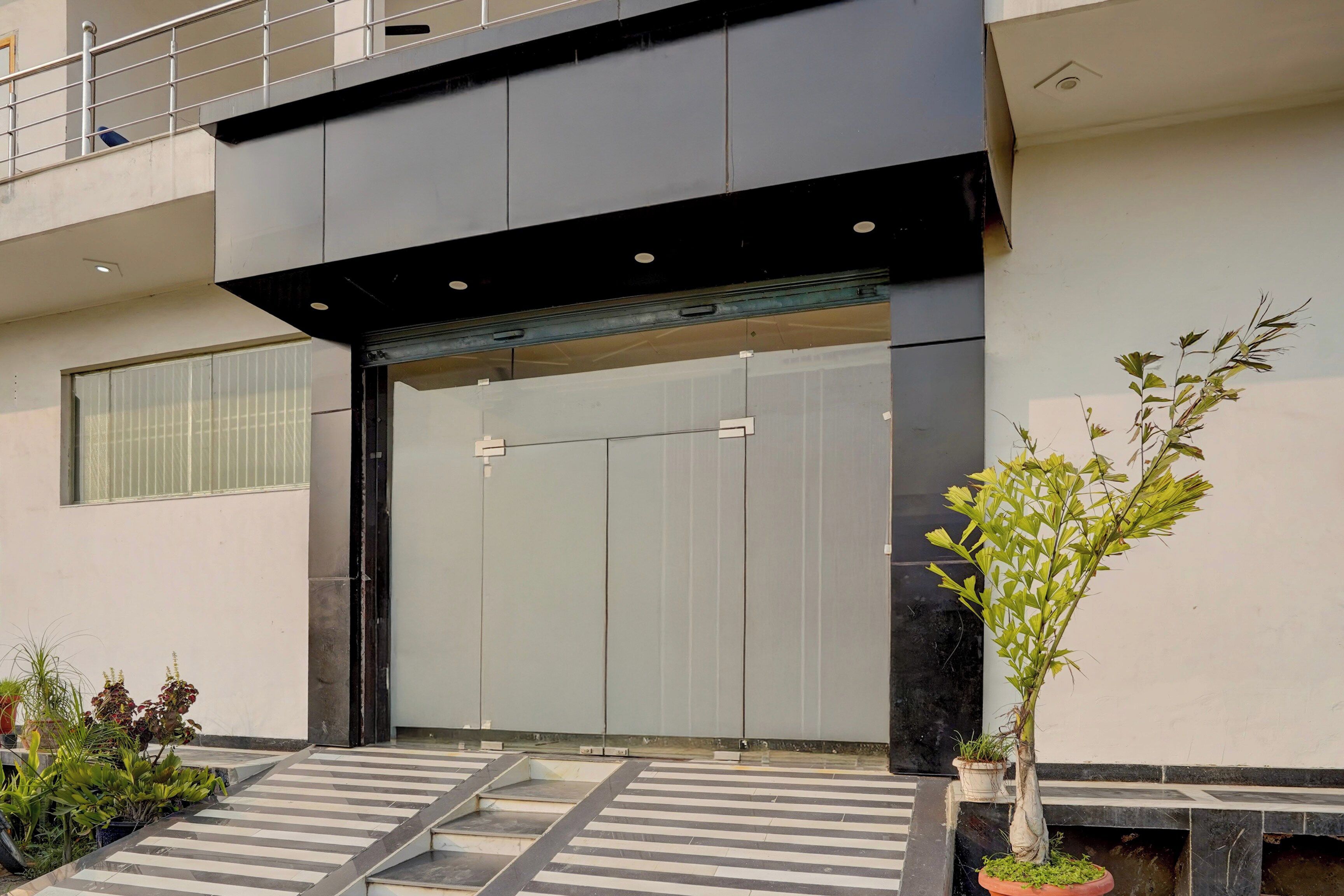 Una entrada moderna de edificio con una puerta grande, una pequeña escalera que sube y plantas en macetas en el suelo.