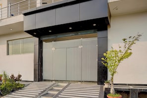 A modern building entrance with a large door, a small staircase leading up, and potted plants on the ground. - Super Hotel O Chhatrapati Shivaji (Meerut)