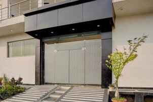 A modern building entrance with a large door, a small staircase leading up, and potted plants on the ground.