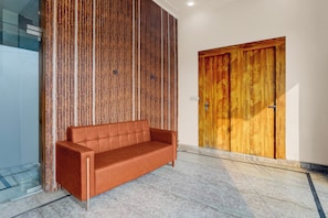 A modern interior with a wooden panel wall, a brown leather sofa, and a wooden door. - Super Hotel O Chhatrapati Shivaji (Meerut)