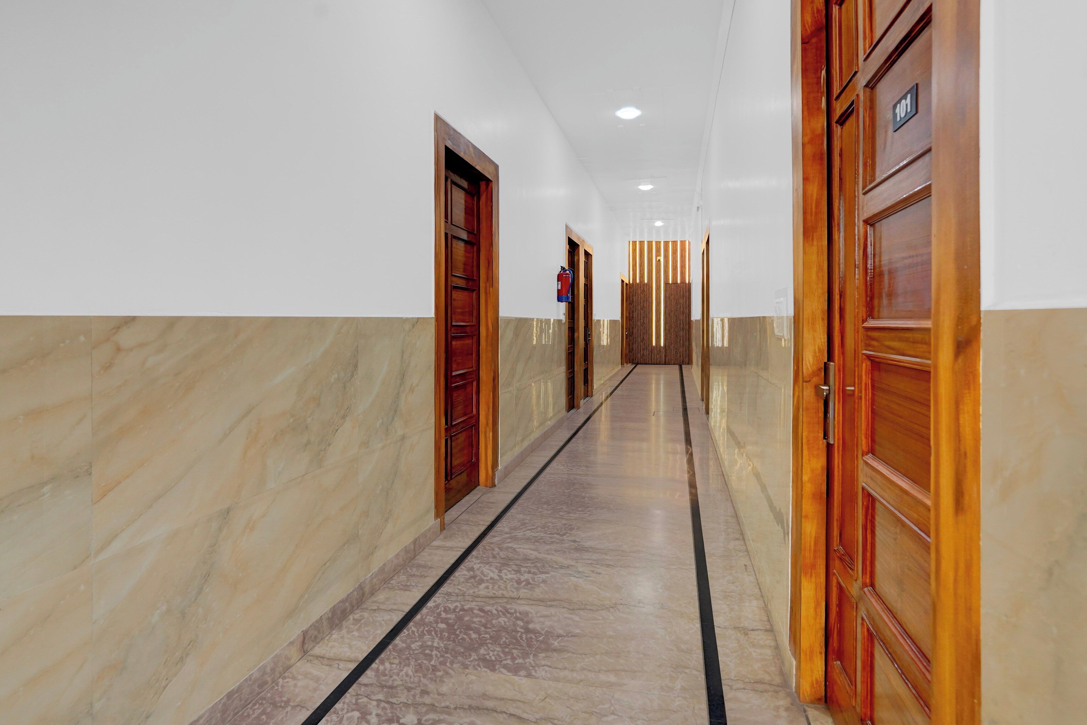 A corridor with marble flooring, wooden doors, and a fire extinguisher on the wall.
