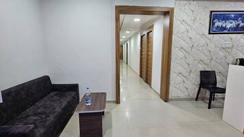 A hotel lobby with a reception desk, a sofa, a water bottle on a table, and a corridor leading to other rooms.