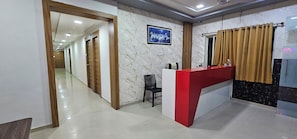 Zona de recepción de un hotel, con mostrador, una silla y un pasillo que da a otras habitaciones.