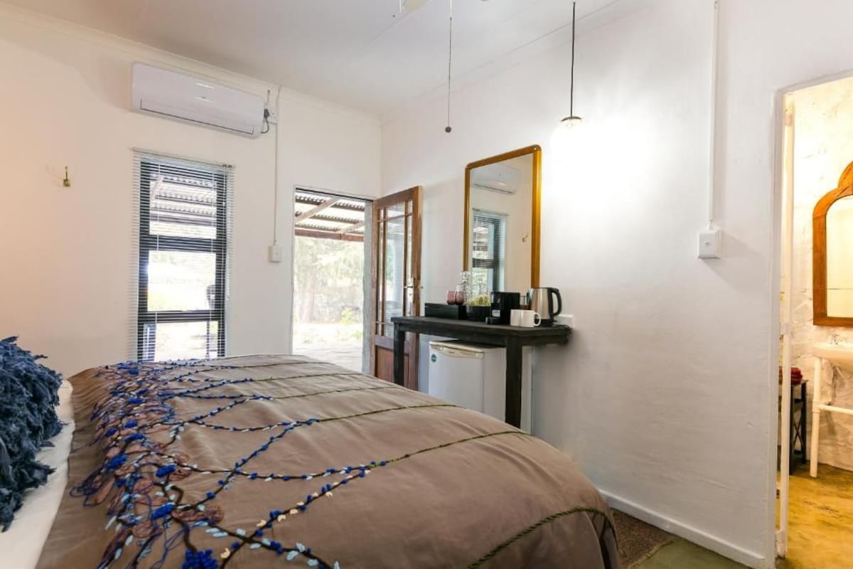 Un dormitorio con cama, mesita de noche, espejo y ventana con persianas.