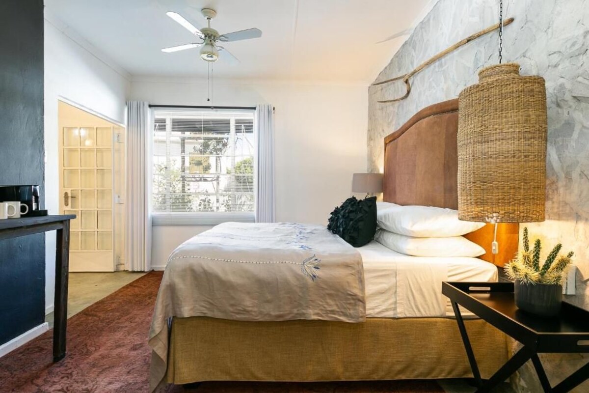 Un dormitorio con una cama, ventilador de techo, ventana, escritorio y lámpara colgante.
