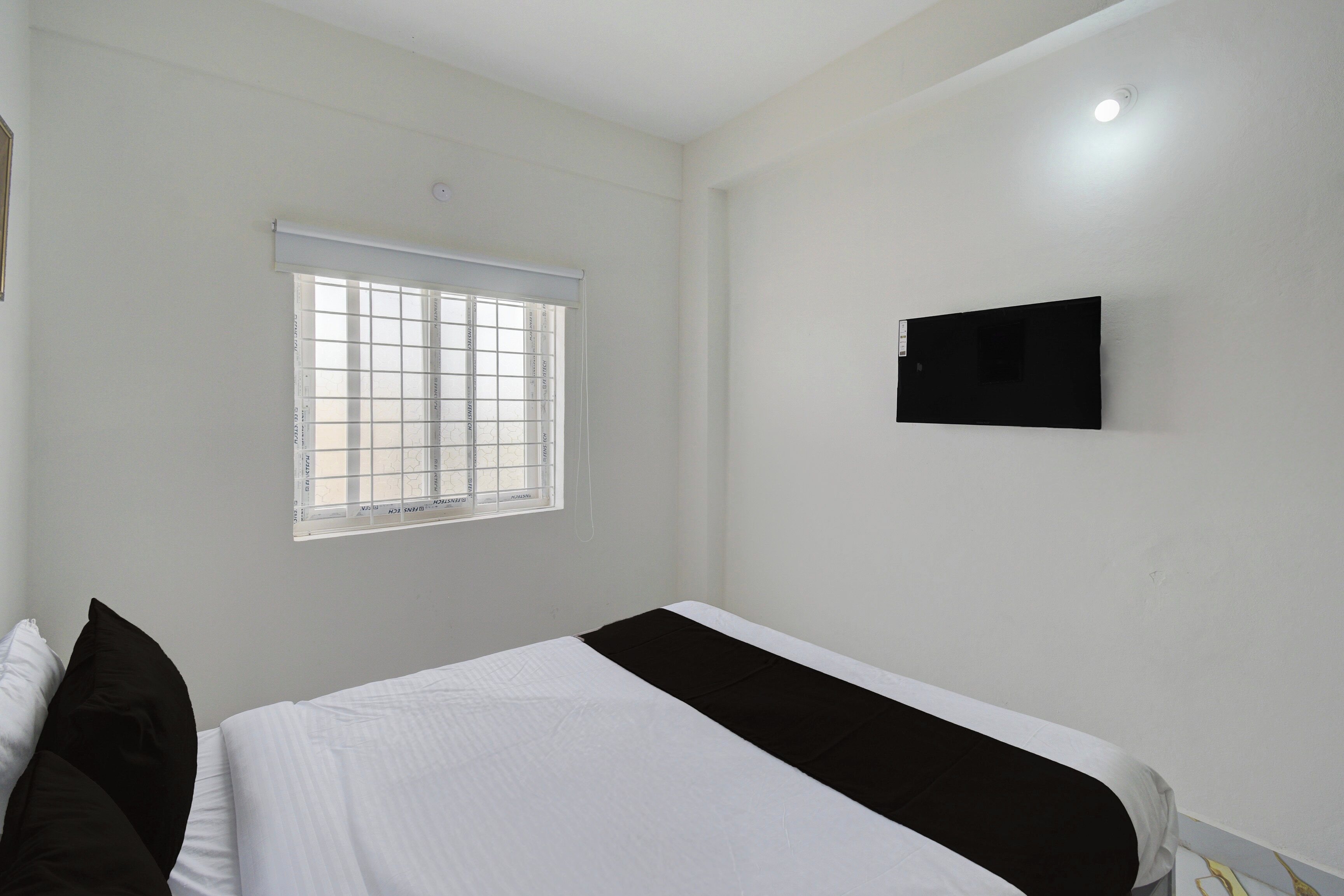 A bedroom with a bed, a window with blinds, and a wall-mounted television.