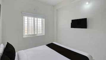 A bedroom with a bed, a window with blinds, and a wall-mounted television.