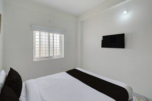 Un dormitorio con cama, una ventana con persianas y un televisor montado en la pared.