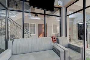 A modern interior with a sofa, a staircase, and a view through large windows. - Super Hotel O Gandimaisamma Thalli (Hyderabad)