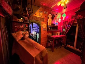 Ein gemütliches Zimmer mit einem Bett, einem Schreibtisch und einer Bar. Es gibt verschiedene Dekorationen und ein Neonlicht.