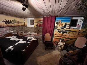Ein Zimmer mit einem Bett, einem Sessel, einem Schreibtisch und einem Wandbild, das eine Wüstenlandschaft zeigt.