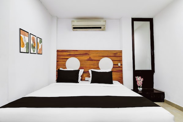 Habitació d'hotel amb llit, panell de capçalera de fusta, aire condicionat fixat a la paret, mirall i obra enmarcades a la paret.