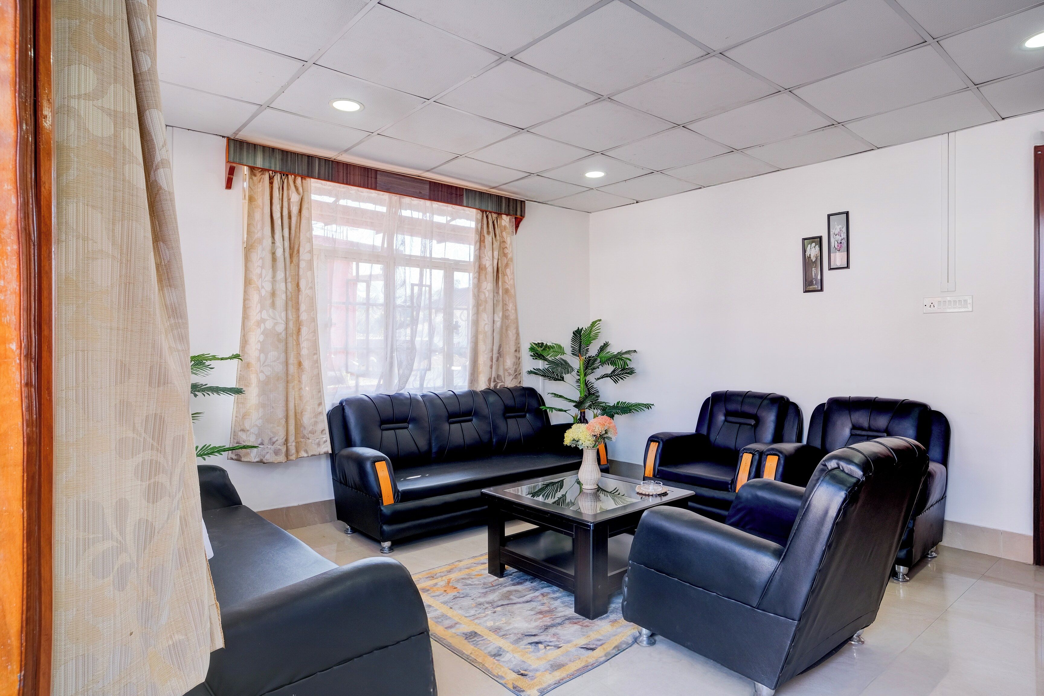 Quarto com sofá de couro preto, duas poltronas de couro preto, mesa de centro de vidro e um vaso com planta.