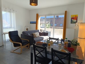 A modern living room with a sofa, a dining table with chairs, and a kitchen area with a refrigerator. - Les Hauts de la Collégiale (4 people) Terrace with a view of Mont Blanc & free parking. (Sallanches)