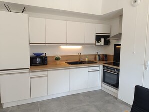A modern kitchen with white cabinetry, a black stove, and a wooden countertop. - Les Hauts de la Collégiale (4 people) Terrace with a view of Mont Blanc & free parking. (Sallanches)