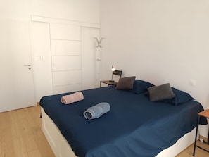 Ett sovrum med en säng, kuddar, ett nattduksbord, en lampa och en klädhängare.