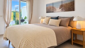 A bedroom with a large bed, two bedside lamps, a view of the outdoors, and a painting on the wall. - Garden apartment in La Cala Sunset (Mijas Costa)