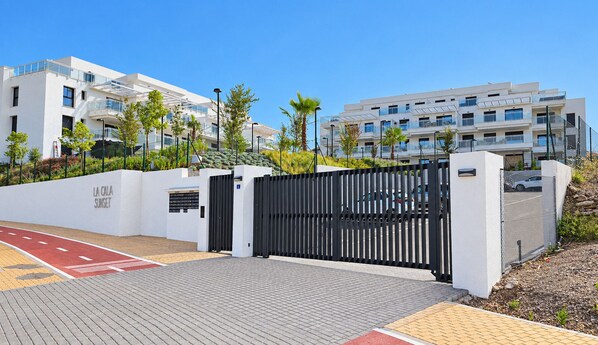 A gated entrance to a modern building complex with a clear pathway and a red bicycle lane. - Garden apartment in La Cala Sunset (Mijas Costa)