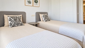 Hotellihuoneessa on kaksi sänkyä, joissa kummassakin on tyyny ja peitto. Sänkyjen välissä on pieni pyöreä pöytä.