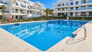 A swimming pool with a metal ladder, surrounded by a fence, and adjacent to a multi-story building with balconies. - Garden apartment in La Cala Sunset (Mijas Costa)
