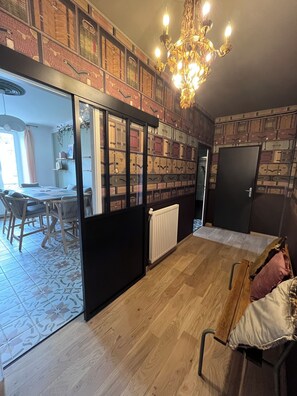 Une pièce dotée d’une grande fenêtre, d’un lustre, d’un plancher en bois et d’un mur où sont posées des valises.