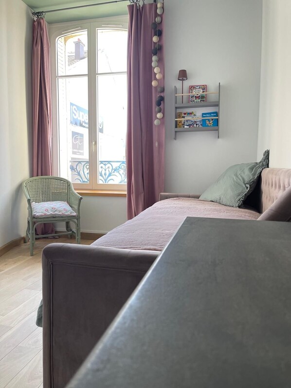 Une pièce comprenant un lit, une chaise, une fenêtre avec des rideaux et une étagère avec des livres et une lampe.